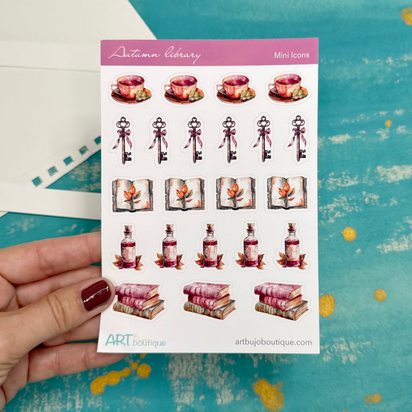 Sheet of decorative stickers with autumn-themed designs held by a hand on a blue background.