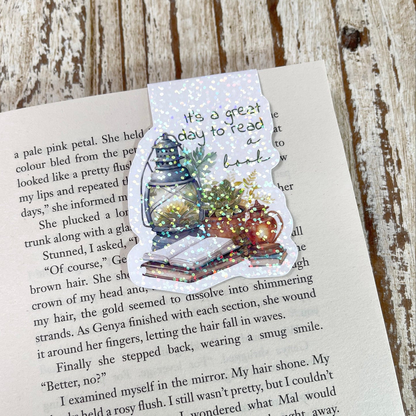 A die-cut sticker featuring a Christmas tree, Santa Claus, and a message about reading, placed on an open book page over a rustic wooden surface.