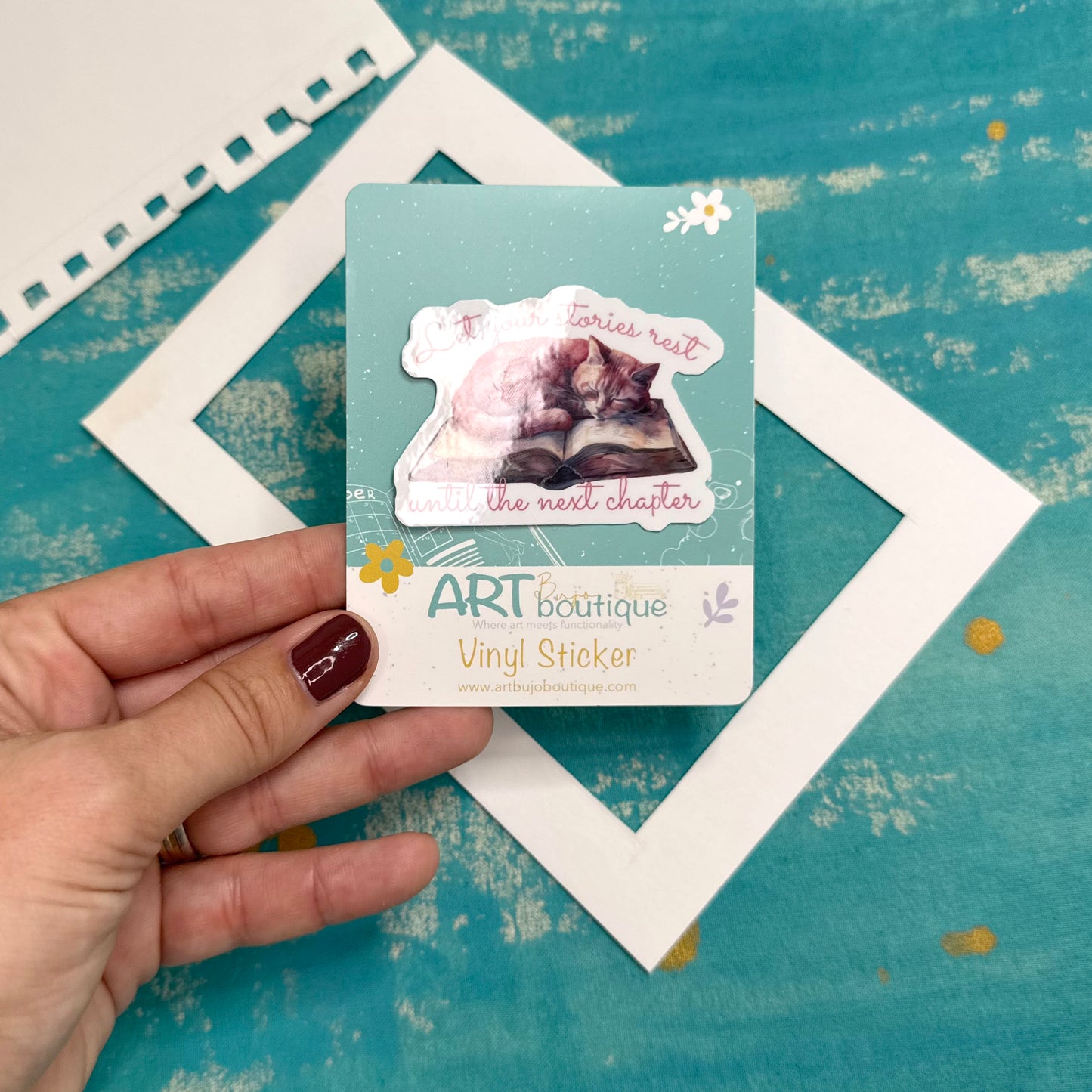 Hand holding a vinyl sticker card with a cat design on a textured blue background