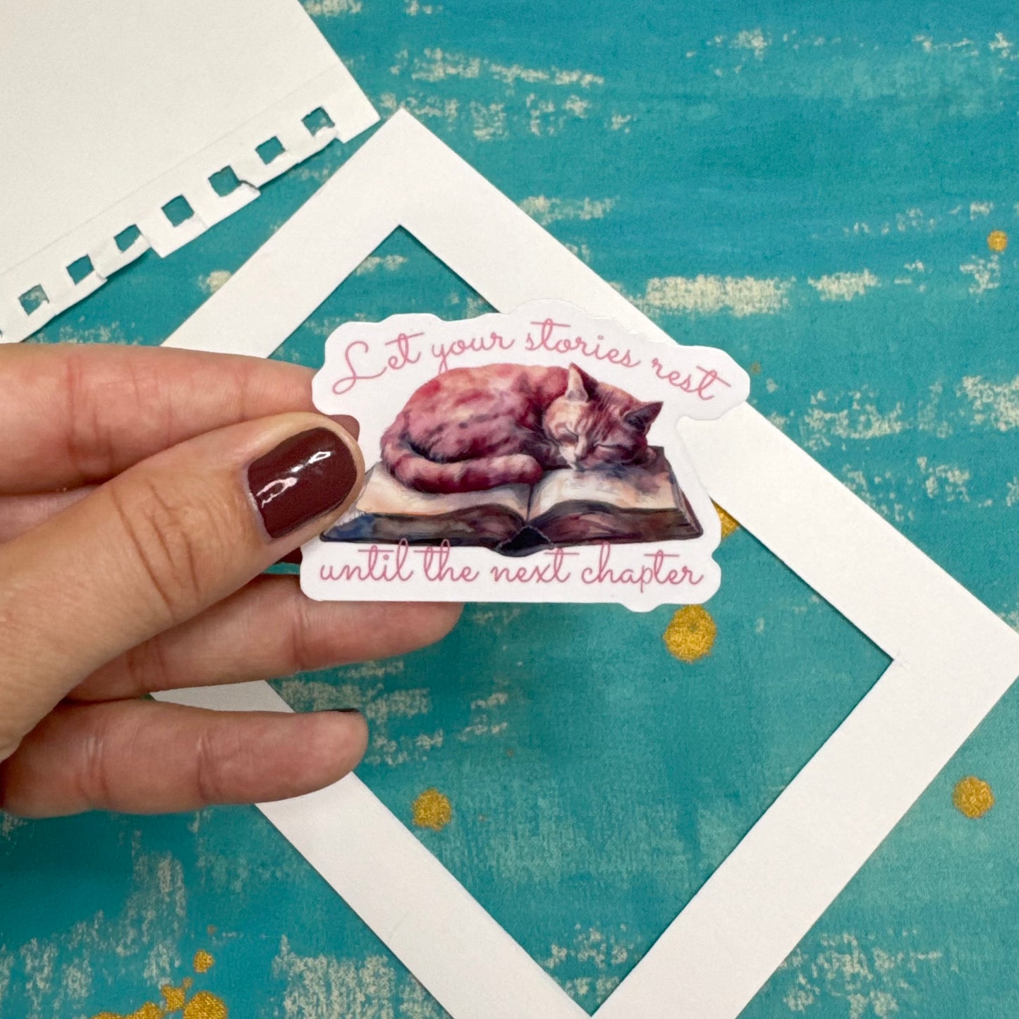 Hand holding a sticker with a cat illustration and text on a textured blue background