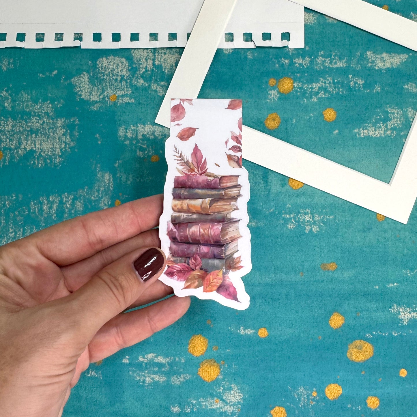 Hand holding a colorful sticker with floral design on a textured teal background