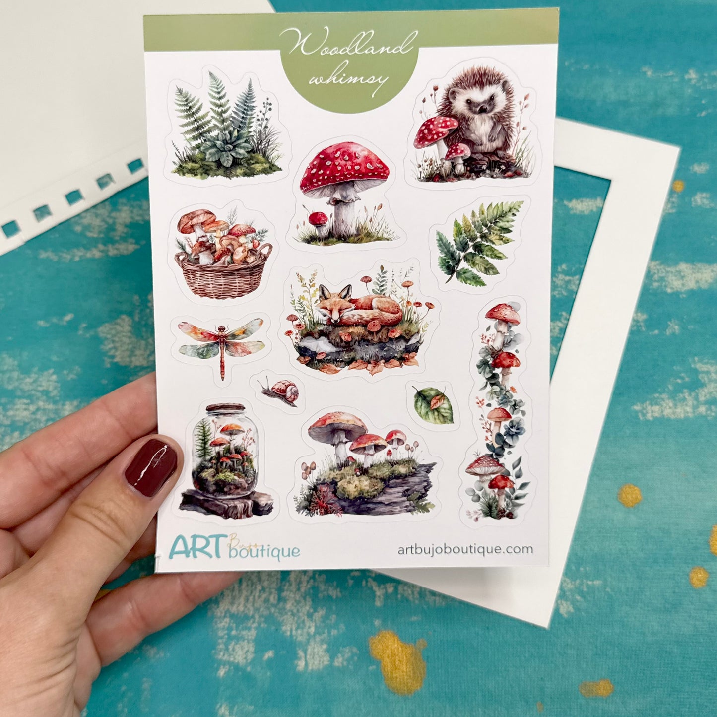Sheet of nature-themed stickers held by a hand on a blue surface with 'ART boutique' branding.