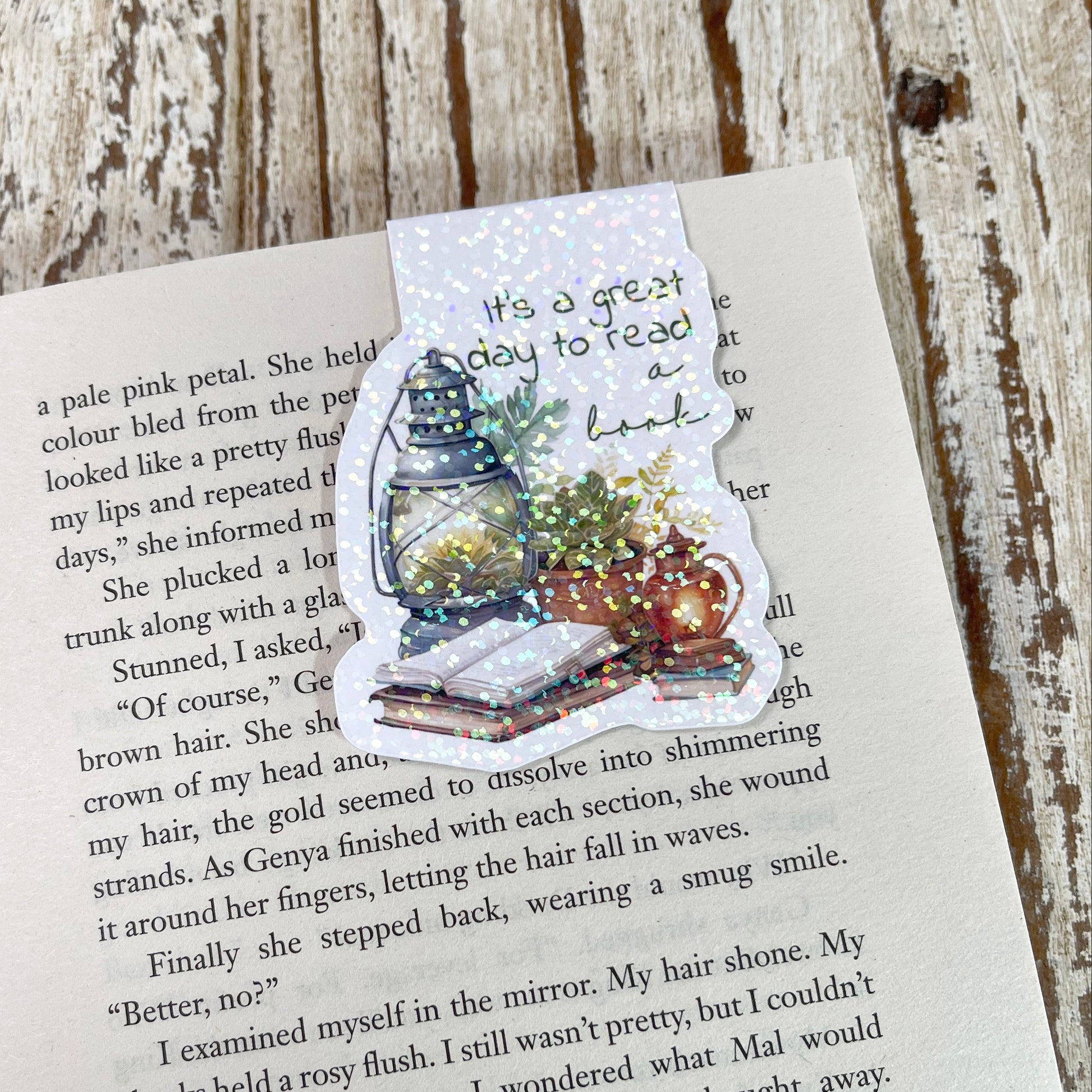 A die-cut sticker featuring a Christmas tree, Santa Claus, and a message about reading, placed on an open book page over a rustic wooden surface.