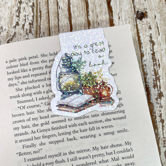 A die-cut sticker featuring a Christmas tree, Santa Claus, and a message about reading, placed on an open book page over a rustic wooden surface.