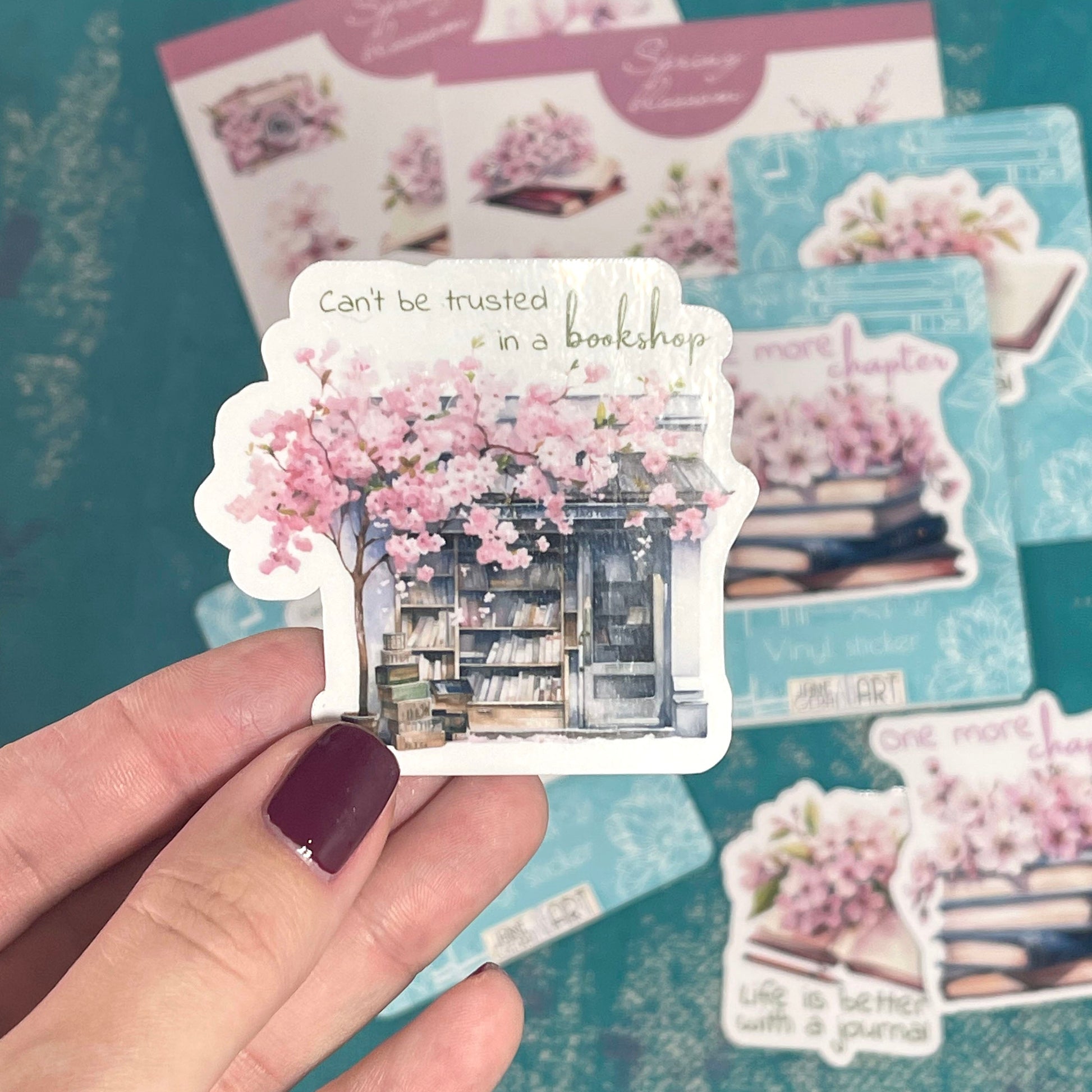 Hand holding a sticker with a bookshop design on a blue textured background with more stickers.