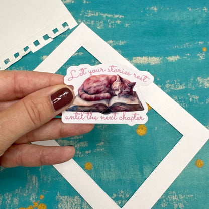 Hand holding a sticker with a cat illustration and text on a textured blue background