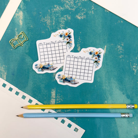 Two decorative planner stickers with floral designs on a textured blue surface with two pencils.