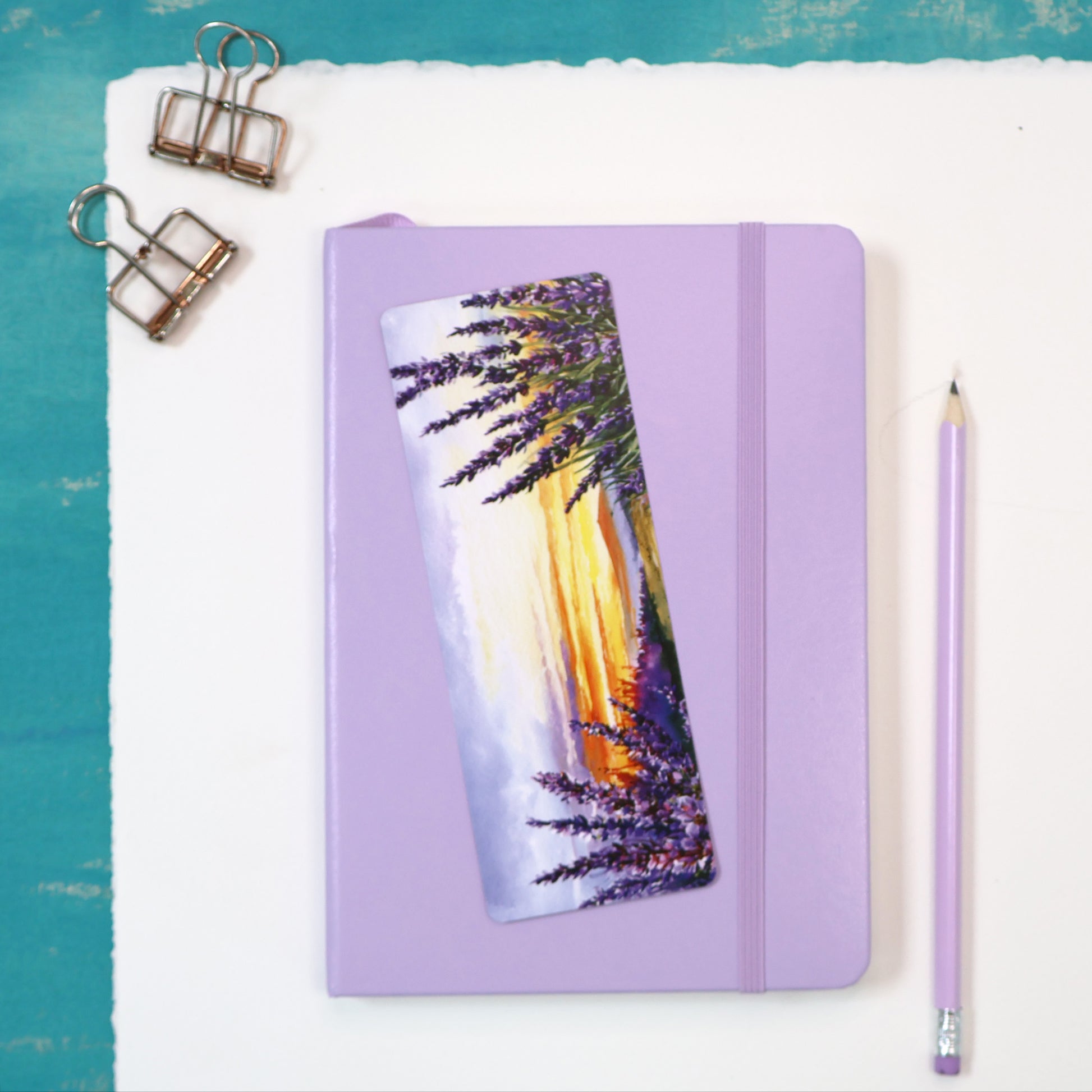 Purple notebook with a scenic bookmark on a white surface with a teal border.