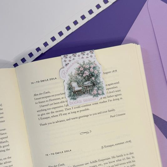 An open vintage-style book with printed text and a small illustrated postcard featuring a woman and children at a table, placed on a purple surface next to a matching envelope.